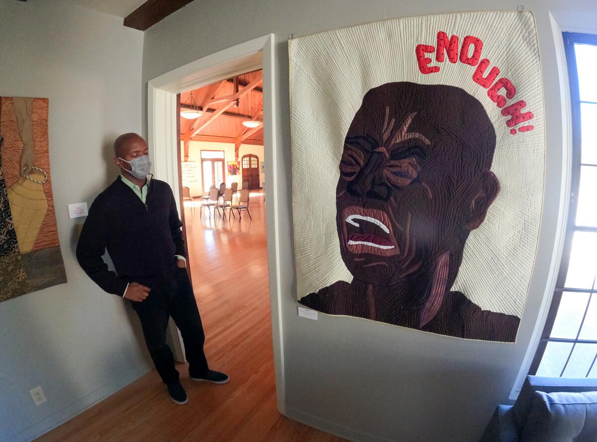 The Rev. Rodrick Echols stands next to one of Allyson Allen's "Piece-ful Protest" quilt works entitled "Enough."
