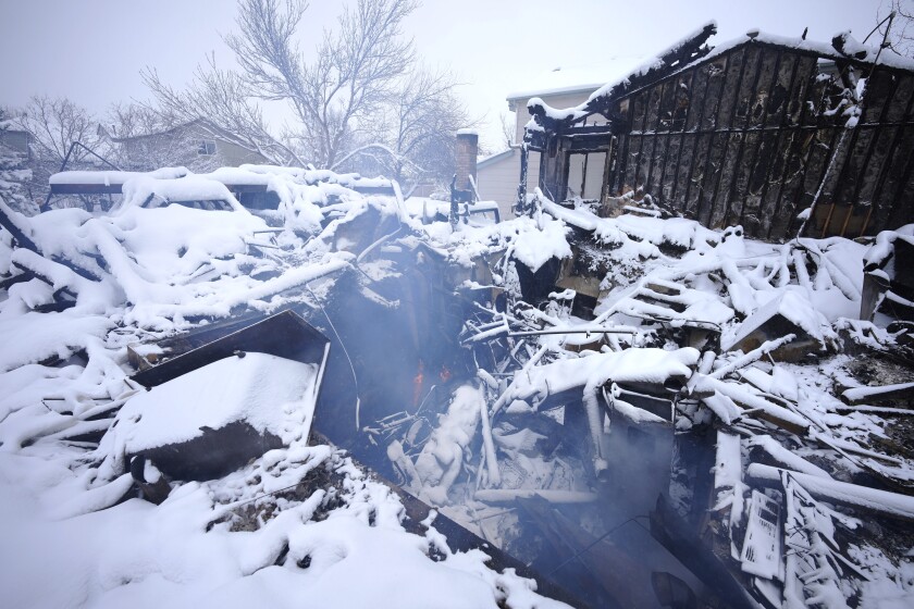 A lone flame flickers as smoke roils from the remains of a home destroyed by a pair of wildfires, Saturday, Jan. 1, 2022, in Superior, Colo. An overnight dumping of snow and frigid temperatures compounded the misery of hundreds of Colorado residents who started off the new year trying to salvage what remains of their homes after a wind-whipped wildfire tore through the Denver suburbs. (AP Photo/David Zalubowski)
