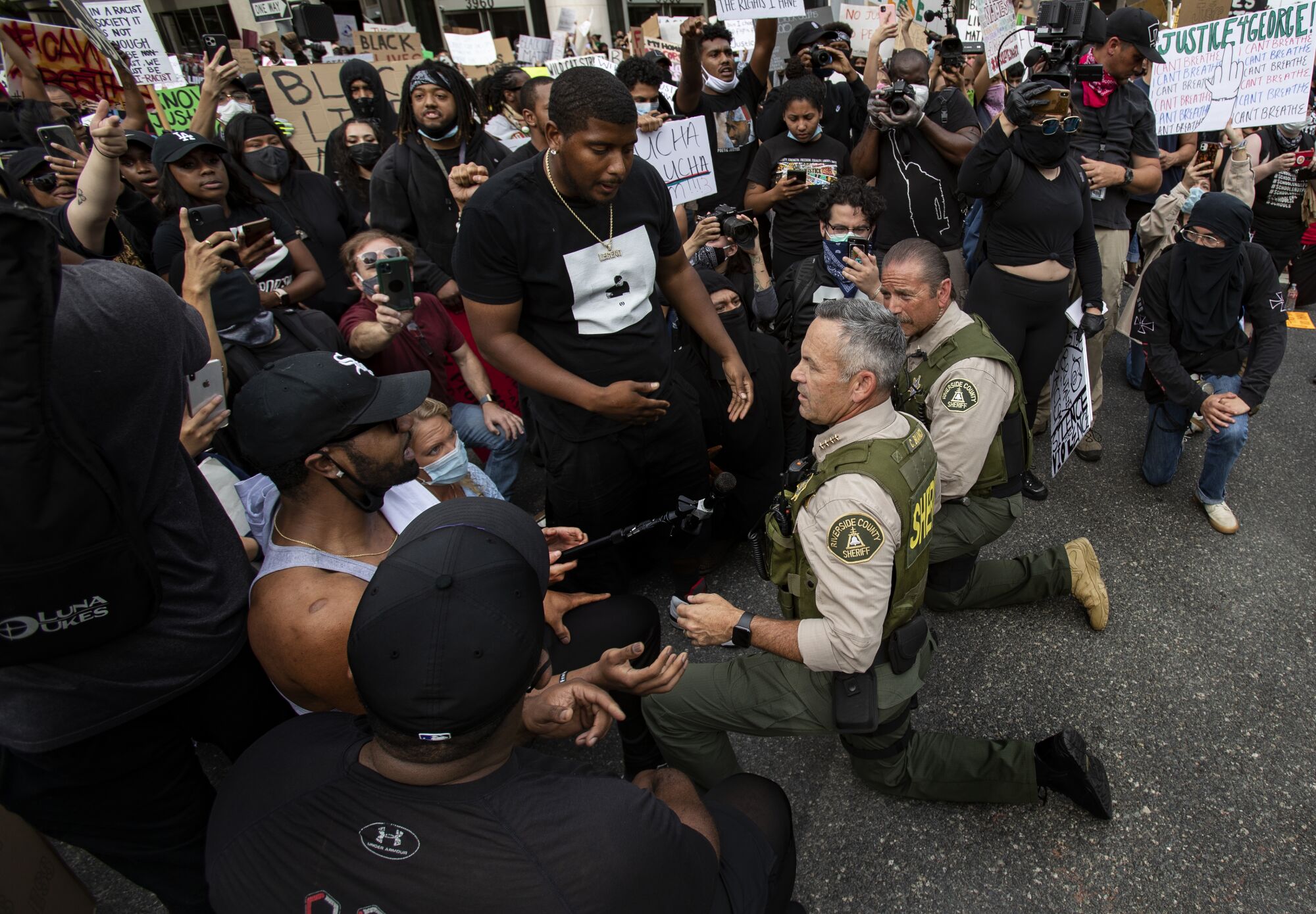 Riverside County Sheriff Chad Bianco takes a knee with demonstrators after thousands of protesters marched.