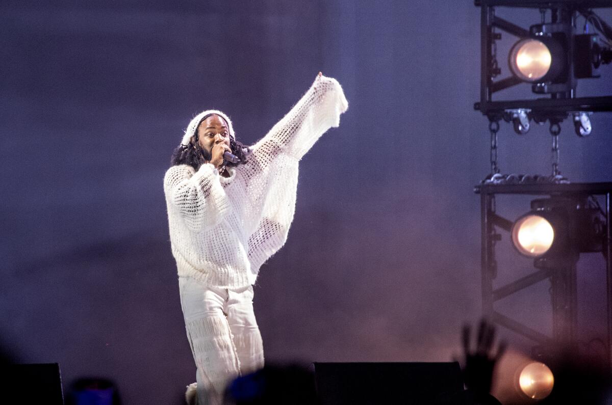 A man in all-white raises his arm while performing on stage. 