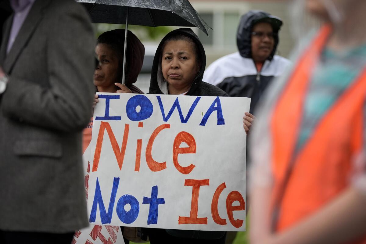 A woman under an umbrella holds a sign that says, "Iowa Nice, Not ICE"