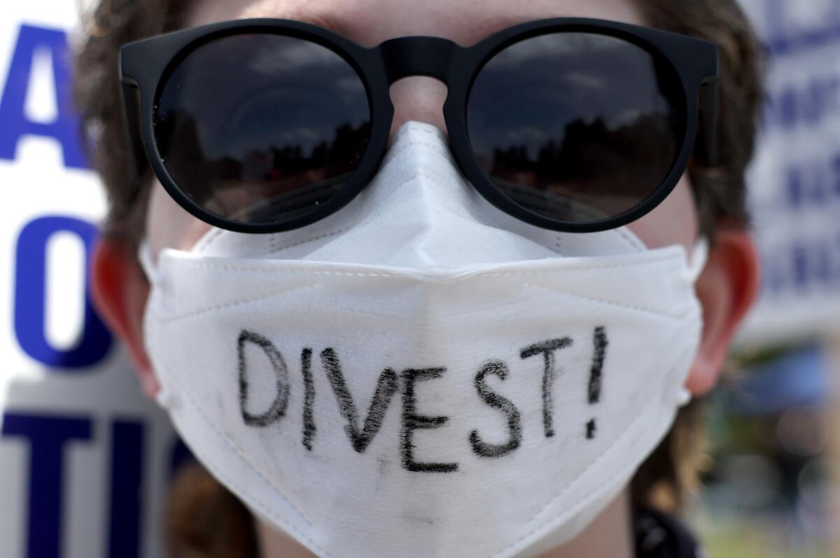 A protester wears a mask with 'divest' written on it