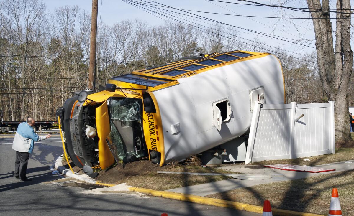 An investigator examines an overturned school bus resting on a fence after colliding with a commuter bus in Old Bridge, N.J. The New York City-bound commuter bus and the school minibus crashed on a state highway, injuring at least 19 people, two critically. School officials said no students were on the school bus, which landed on its side along Route 9.