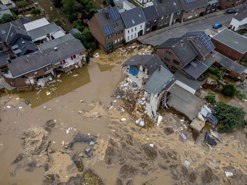 Muddy water fills streets between homes destroyed by flooding in overhead view.