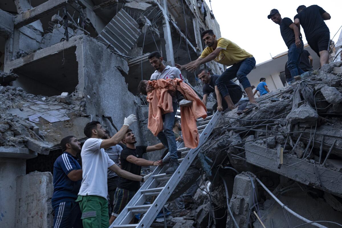 Several men reach out to help as a man carries a small child in bedding down a ladder from the rubble of a destroyed building