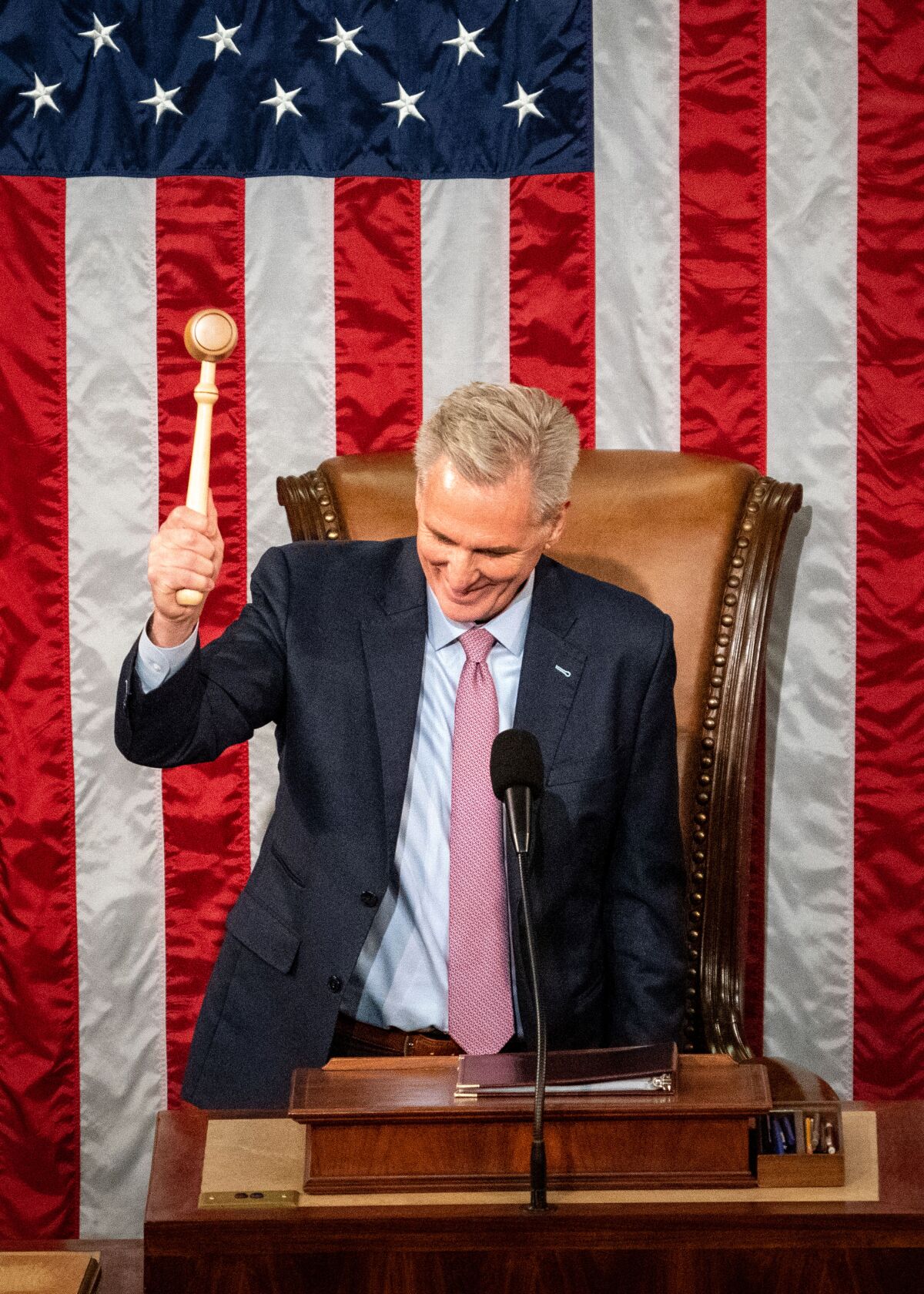 A man lowering a gavel as he stands at a lectern in front of a U.S. flag