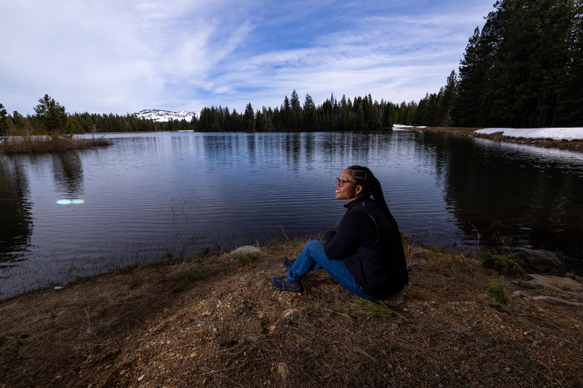 A woman sits beside a lake.