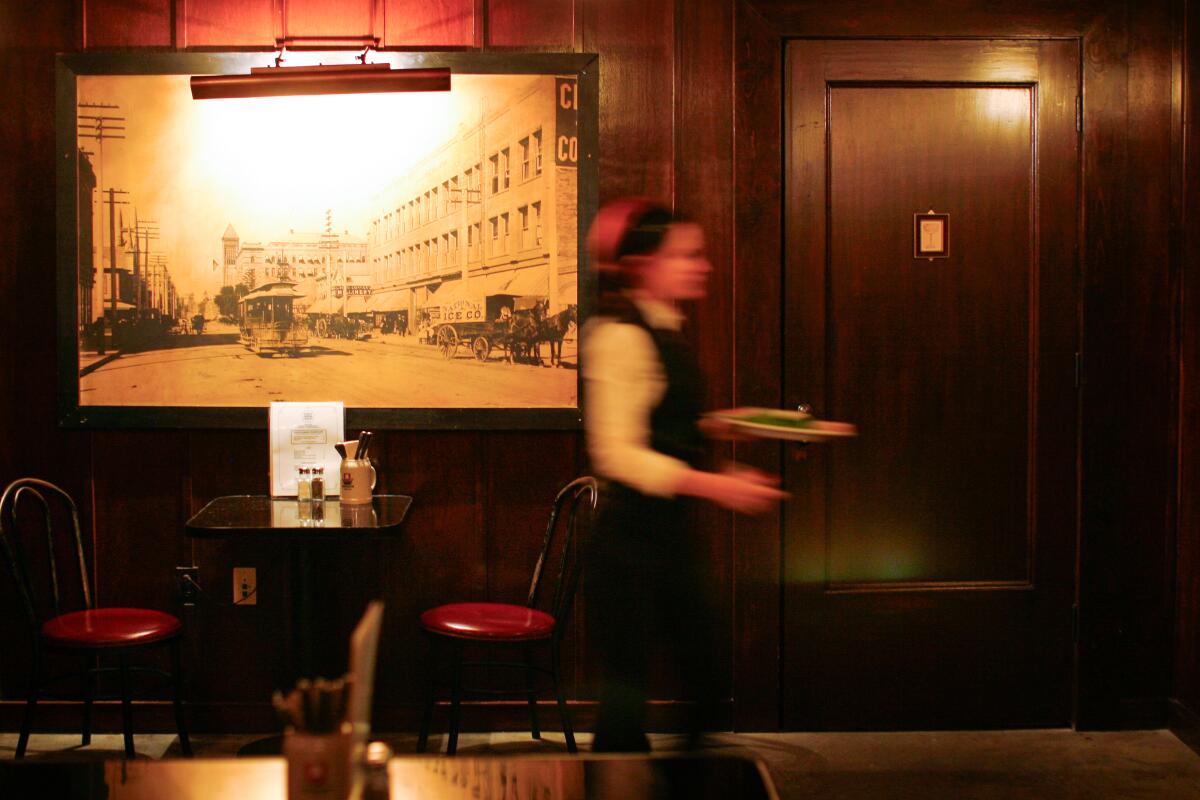 Un camarero caminando frente a una pared con una fotografía en blanco y negro de la ciudad y una sencilla puerta.