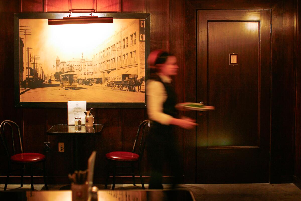 A server walking in front of a wall with a black and white photo of a city and a simple door.