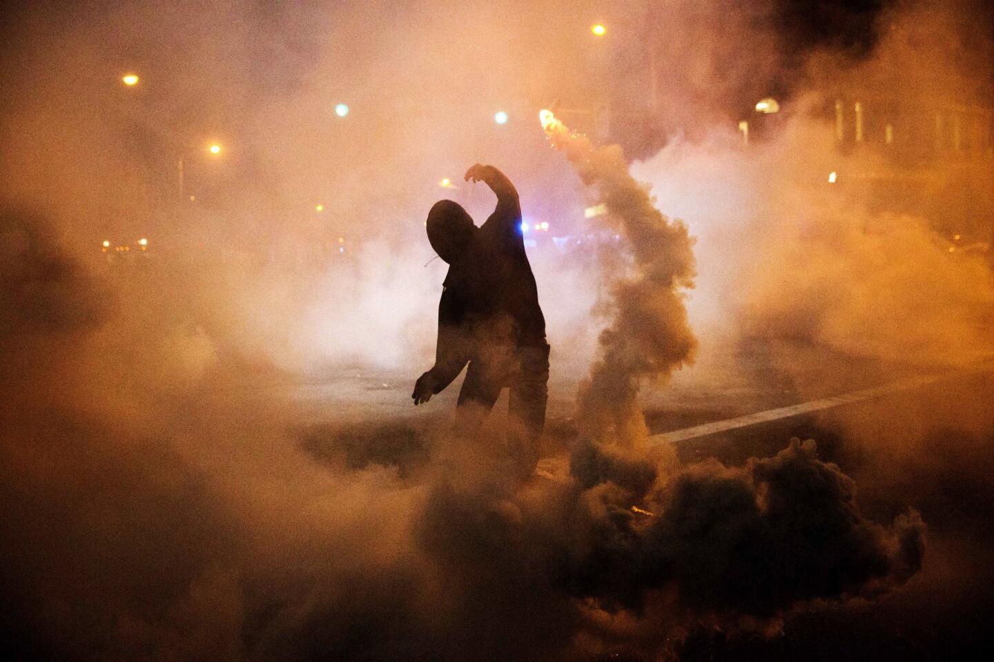 A protester throws a tear gas canister back toward riot police after a 10 p.m. curfew went into effect in the wake of Monday's riots following the funeral for Freddie Gray.
