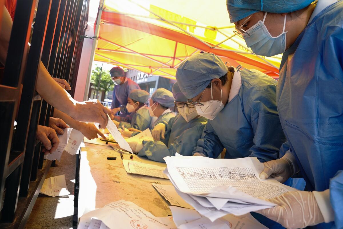 Workers check the names of people waiting to get a COVID-19 test in Beijing.