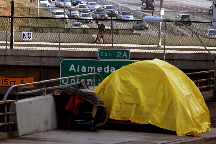 A homeless person takes shelter in a tent along Aliso Street above the 101 Freeway in downtown Los Angeles.