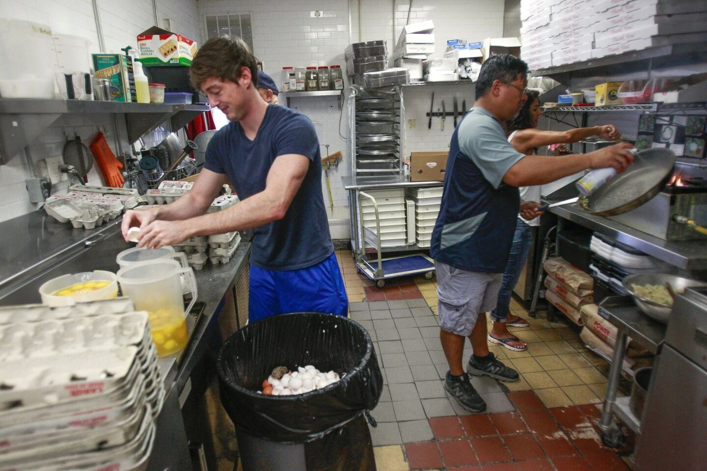 Burrito Boyz volunteer Conor McElroy, left, cracks eggs for scrambling as Jeff Chinn, right, and Mehrnaz Johnson cook scrambled eggs to make egg burritos for homeless people.
