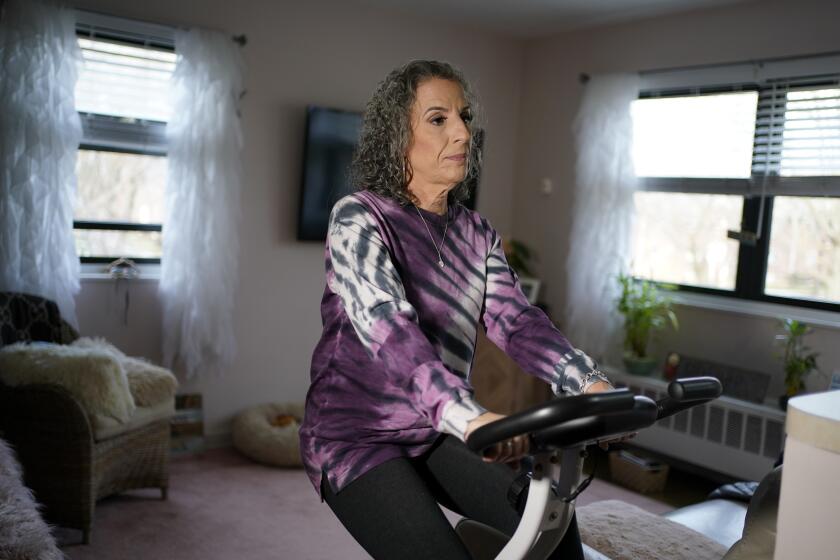 Catherine Busa se ejercita en una bicicleta estática en su casa de Nueva York el 13 de enero del 2021. Busa contrajo el COVID-19 y sobrevivió, pero ocho meses después sigue sintiendo algunos síntomas. (AP Photo/Seth Wenig)