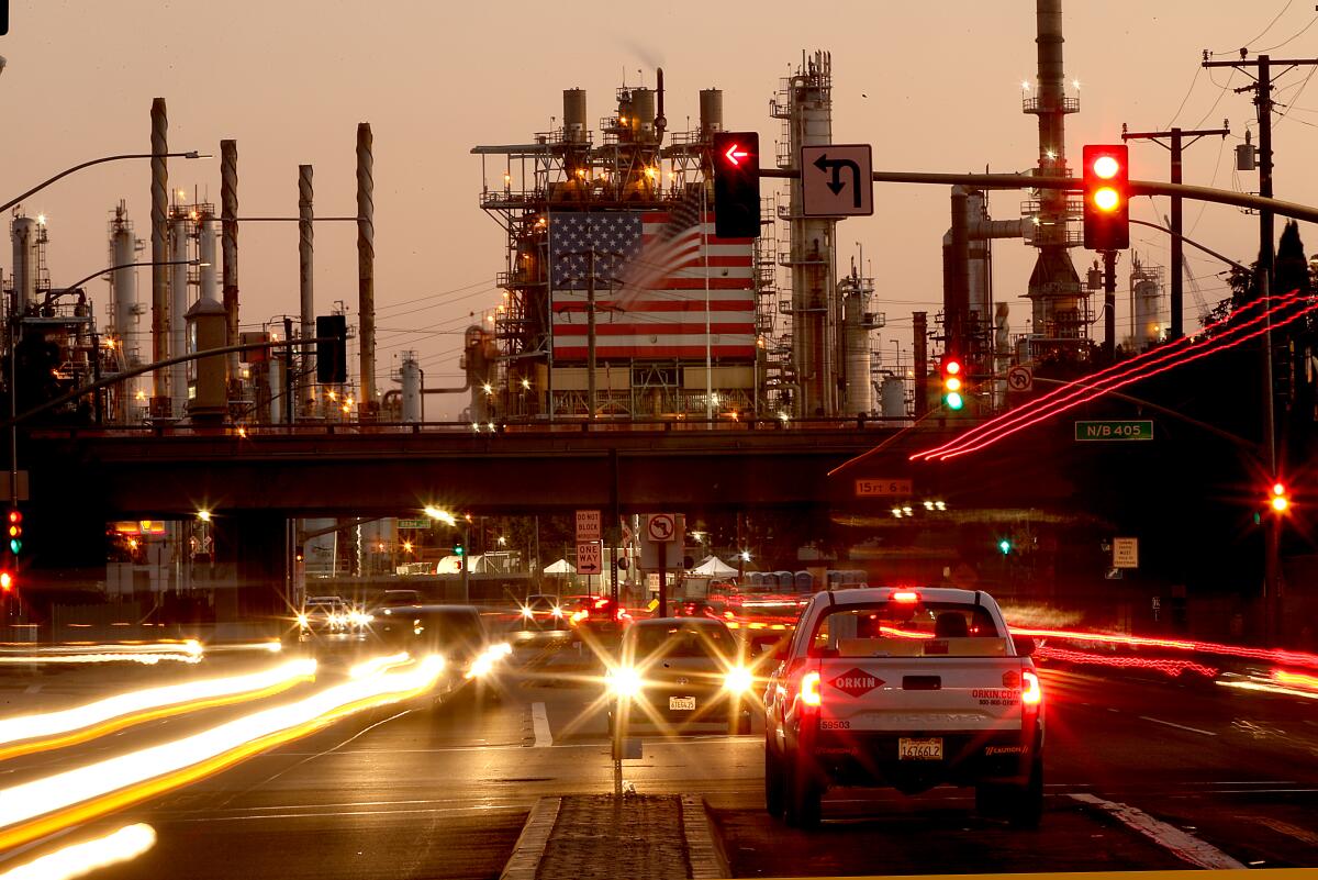 Traffic streams past a refinery draped with an American flag.