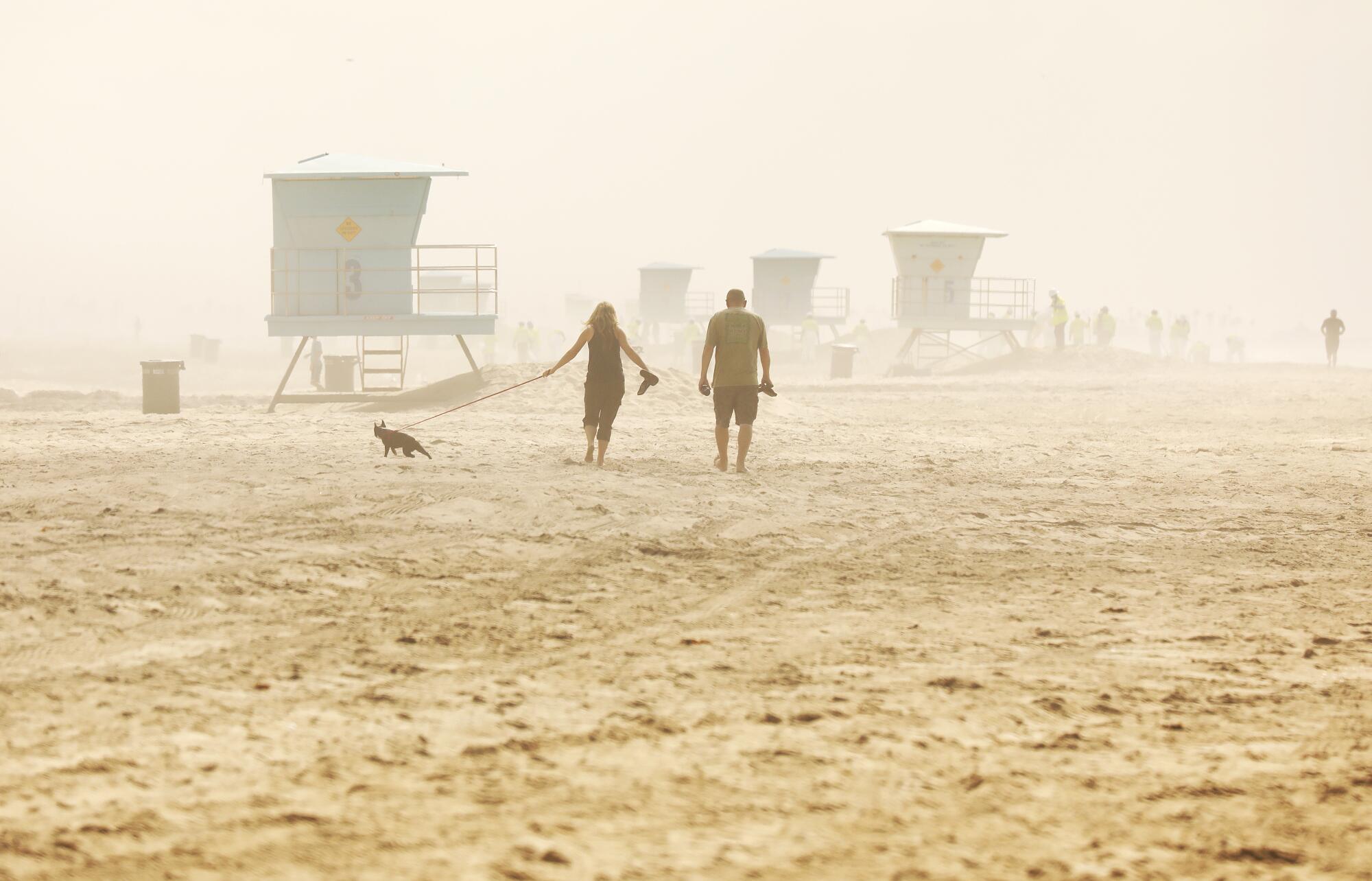 People walk the beach under partly cloudy skies atHuntington Beach