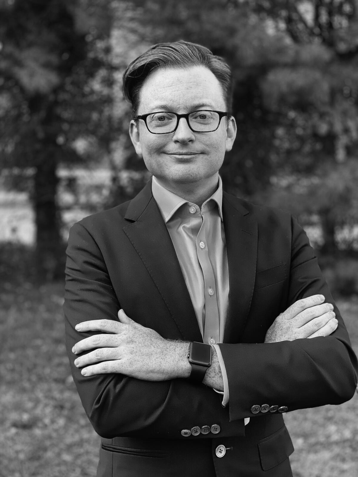 A black-and-white photo of a man with glasses in a button-down shirt and sport coat