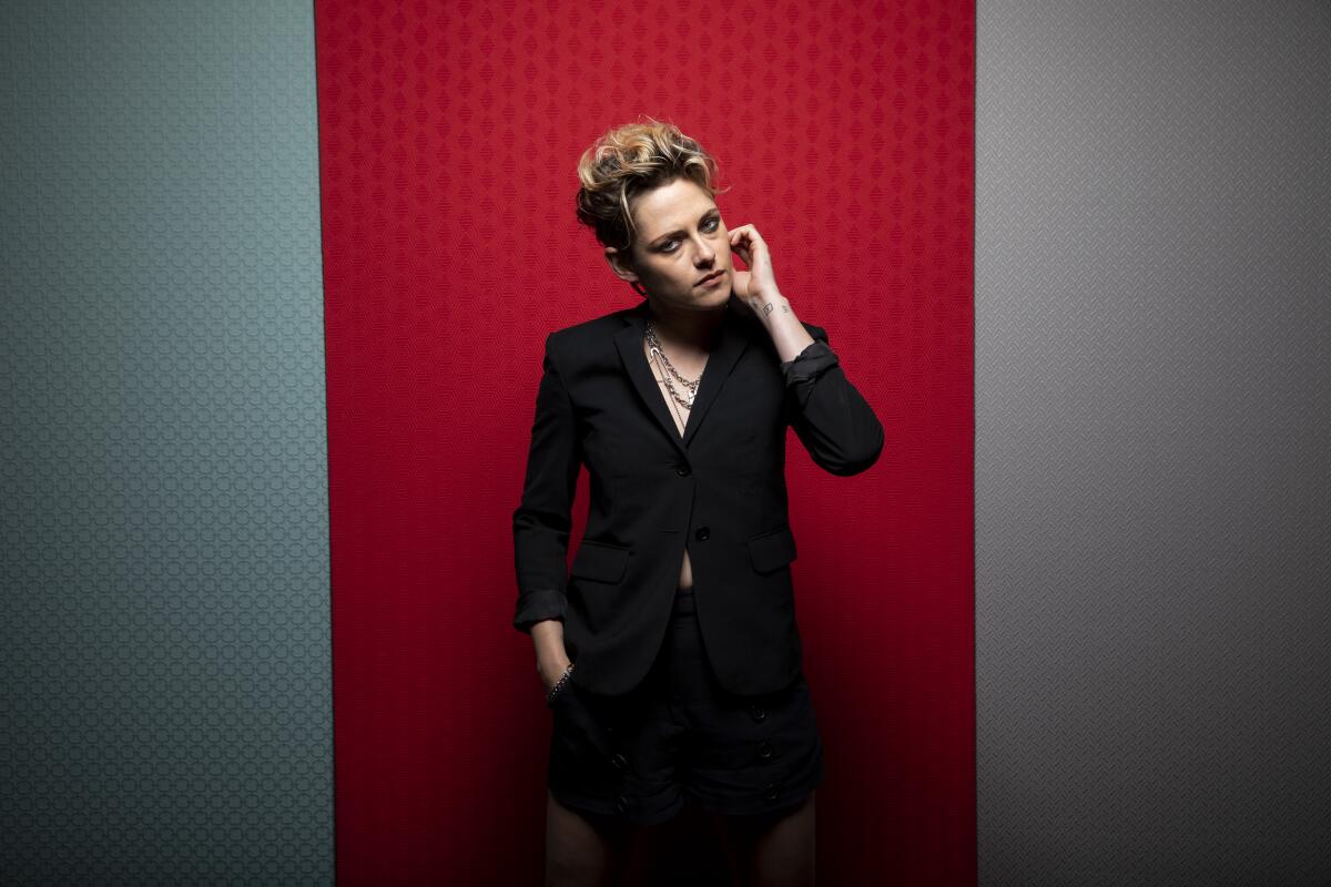 Kristen Stewart poses with her hand on her cheek at the Toronto Film Festival in front of a red and gray backdrop