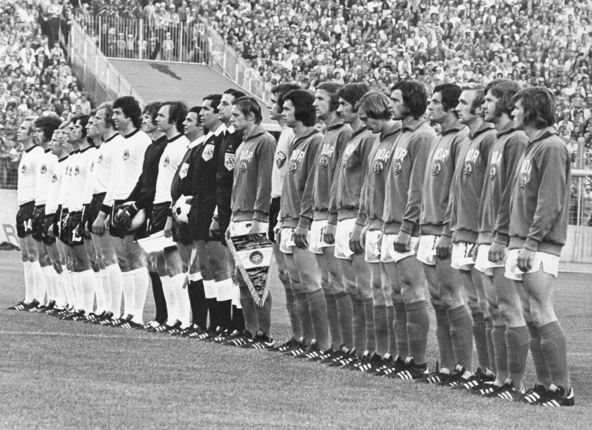 FILE - The teams from West Germany, in white shirts, and East Germany line up for the national anthems before the start of the Football World Cup Group 1 match at the Volksparkstadion, in Hamburg, on June 22, 1974. East German captain Bernd Bransch at center holding flag. Bernd Bransch, who captained East Germany at its only World Cup appearance in a symbolic Cold War win over West Germany, has died. He was 77. Bransch's former club Hallescher FC said in a statement Sunday June 12, 2022 that he had died on Saturday following “a long, severe illness." (AP Photo/File)