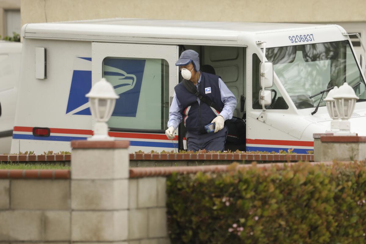 A postal worker wearing a mask and gloves delivers mail in Torrance on March 14.