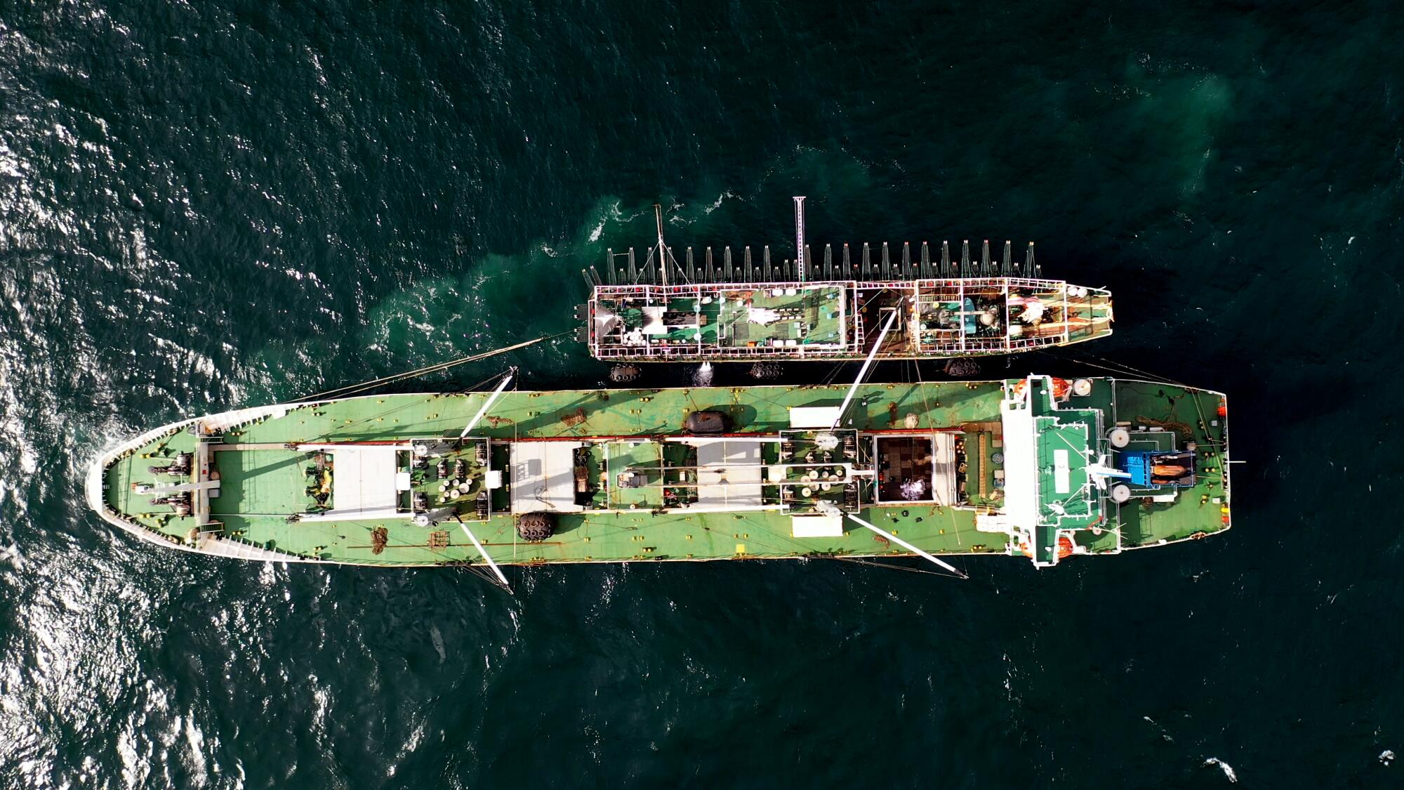 A bird's eye view of a large vessel with a small one alongside it on the ocean 