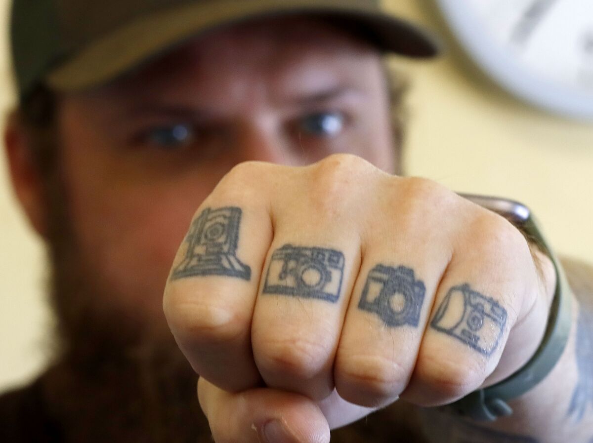 Rob Cowan displays the camera tattoos on the fingers of his left hand.  