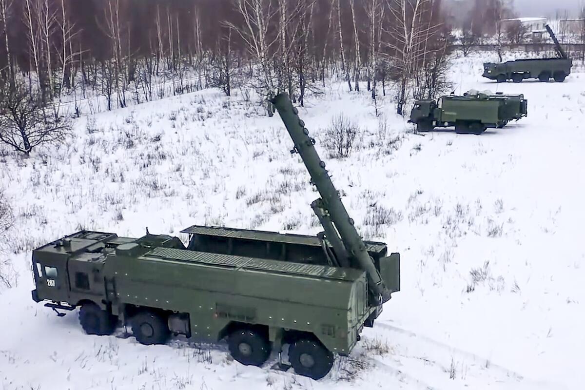 Three green military vehicles with missile launchers in the back sit on a snow-covered landscape with barren trees 