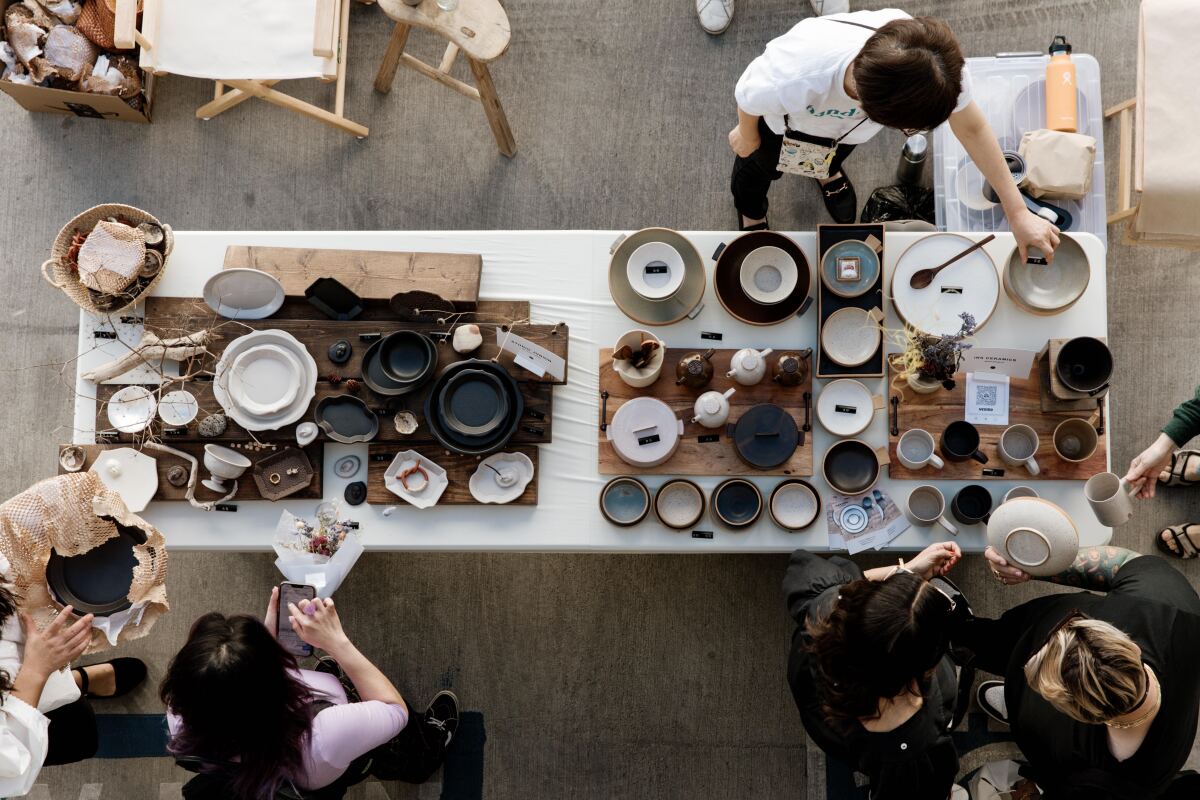 An overhead photo of shoppers perusing a table of ceramic plates, platters, cups and teapots.