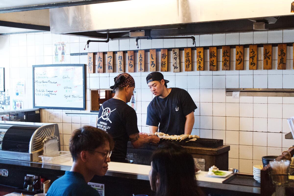 Two employees work the yakitori grill at Shin-Sen-Gumi's original Gardena location. Guests dine at the bar in the foreground.