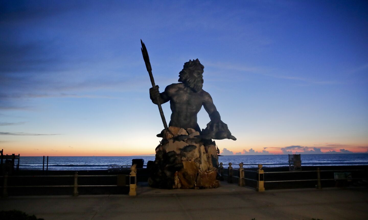 The bronze statue of Neptune stands with the sunrise behind, Wednesday, Sept. 12, 2018, in Virginia Beach, Va., as Hurricane Florence moves towards eastern shore.