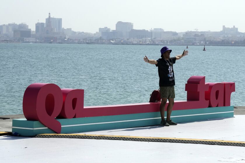 A visitor walks past a photo spot on a street along the beach promenade for Qatar 2022 FIFA World Cup in Doha, Qatar, Monday, Nov. 21, 2022. (AP Photo/Eugene Hoshiko)