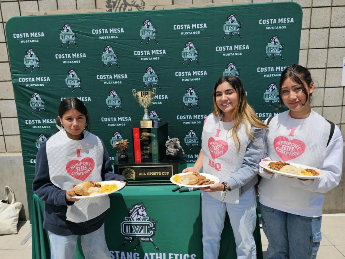 Costa Mesa athletes pose with a plate of food in front of the trophy at the All-Sports Cup luncheon at Costa Mesa High.