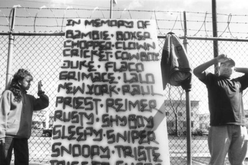Los artistas Erica Parra y Joe Diaz en 1994, con el segmento de una pared que conmemora la muerte de miembros de pandillas durante los seis años anteriores en los complejos de Boyle-Heights-Pico Aliso.