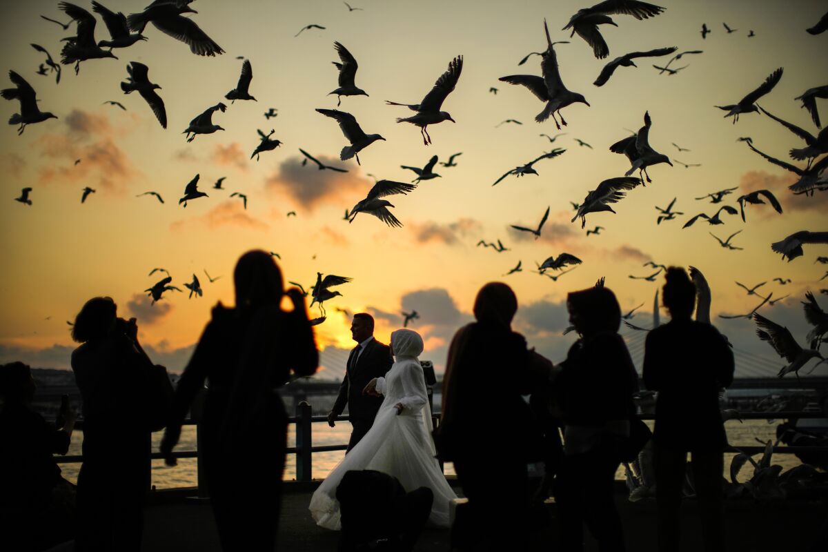 A couple, center, pose during a photo session at the Galata bridge as the sun sets in Istanbul, Turkey, Thursday, July 7, 2022. (AP Photo/Francisco Seco)