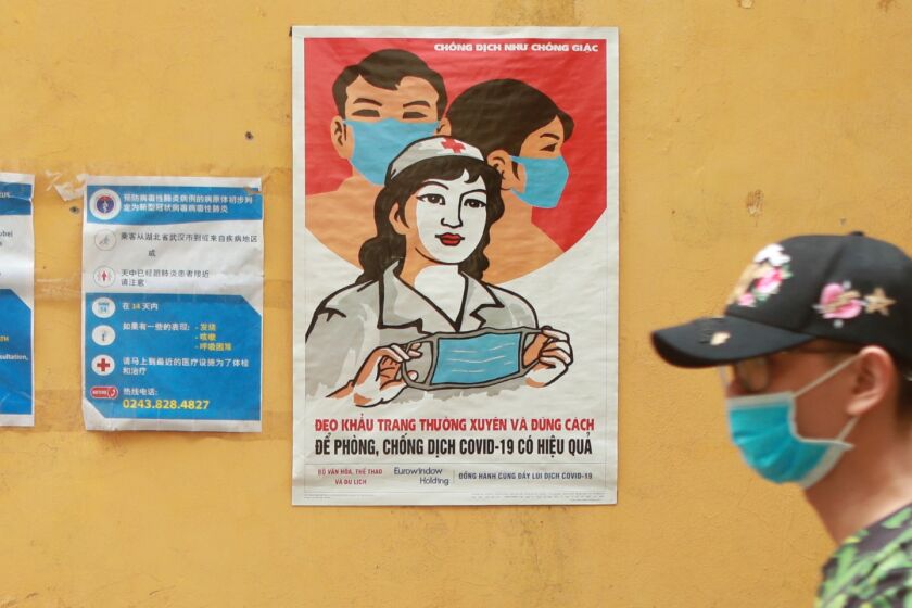 A masked man walks past a poster encouraging people to wear face masks correctly in Hanoi, Vietnam, Thursday, Apr. 23, 2020. Business activities resume in Vietnam as the country lifts the nationwide lockdown to contain the spread of COVID-19.