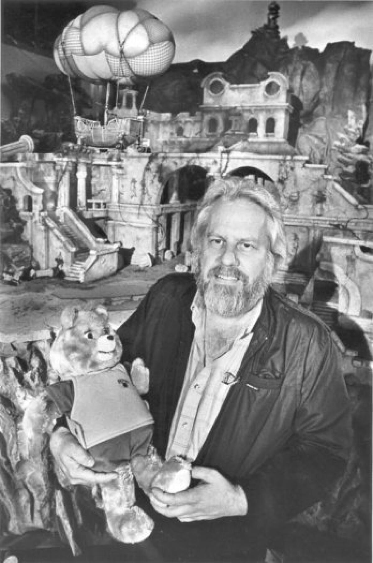 Ken Forsse holding the Teddy Ruxpin character in front of the set of the Hard to Find City, part of the adventures of the Ruxpin character being filmed at Renmar Studios in Hollywood.