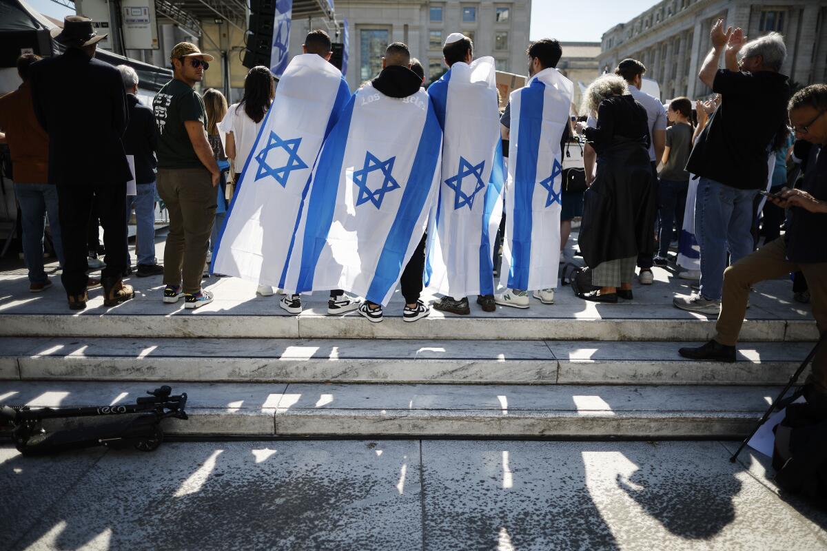 Four people draped with Israeli flags stand among a crowd 