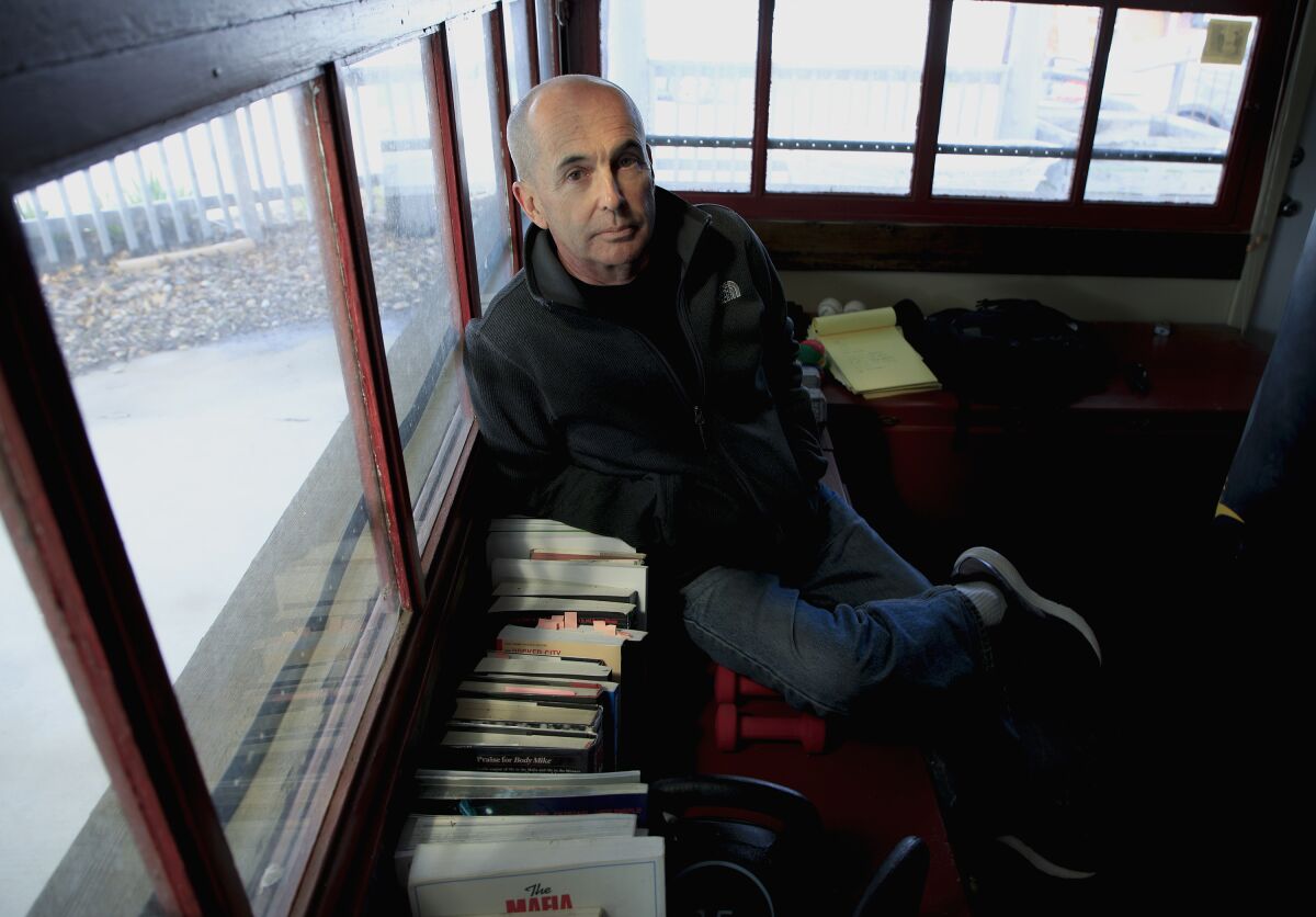 Don Winslow sits on a bench next to books.