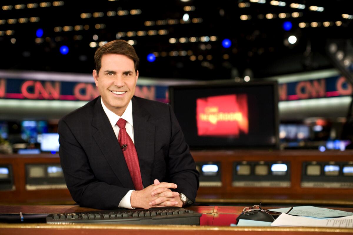 Newscaster with red tie sitting at a desk