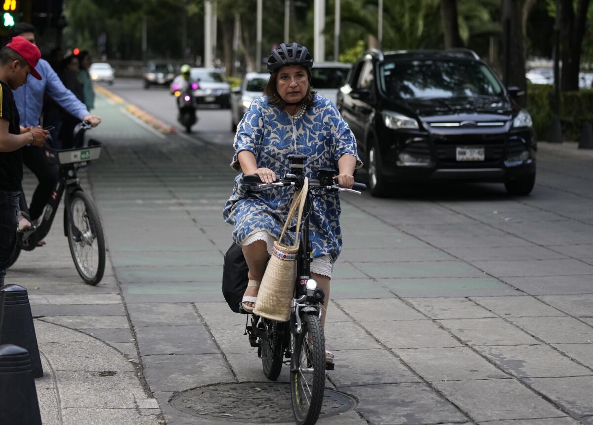 A woman wears a helmet and dress as she rides a bike in traffic.
