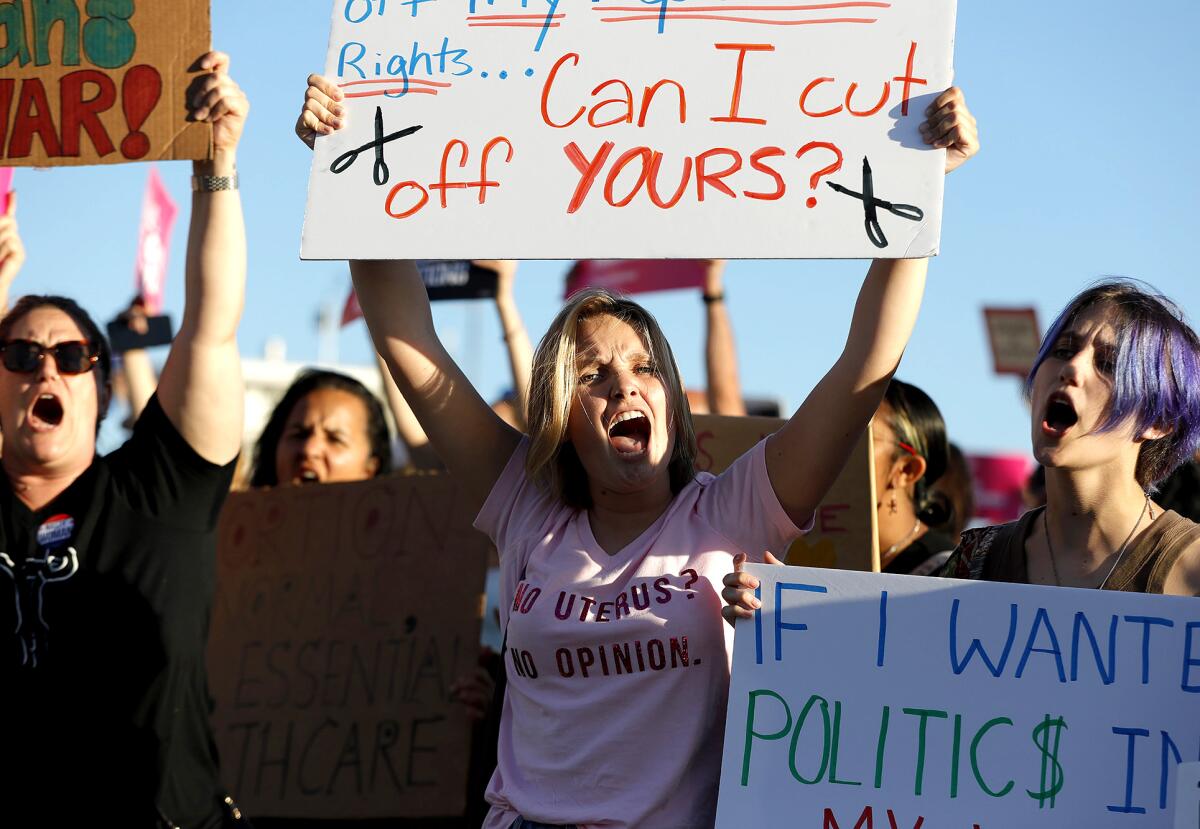 A woman in a pink shirt that says "No uterus? No opinion" shouts and holds up a protest sign among a crowd
