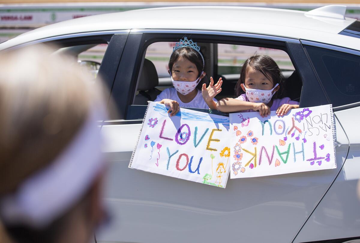 Abigail and Elia Choi, 5, hold signs and wave to staff members at Mariners Christian School during "The Great MCS Drive-Bye," a socially distanced celebration on the last day of school on Friday.