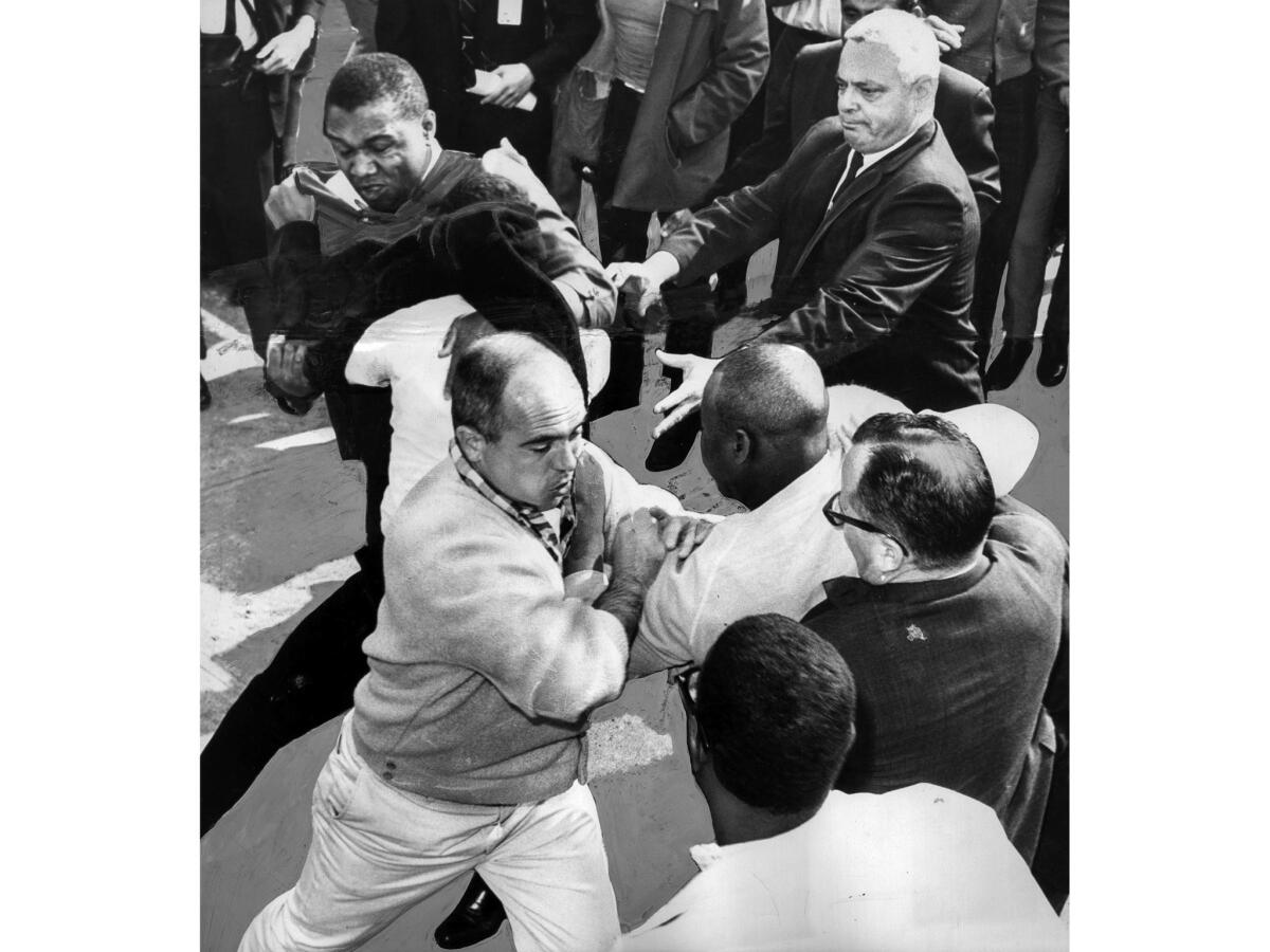 March 10, 1965: Three U.S. Marshals – one in the photo's upper left, one wearing a checkered shirt at lower left, and one in upper right – struggle with demonstrators blocking entry to L.A.'s Federal Building.