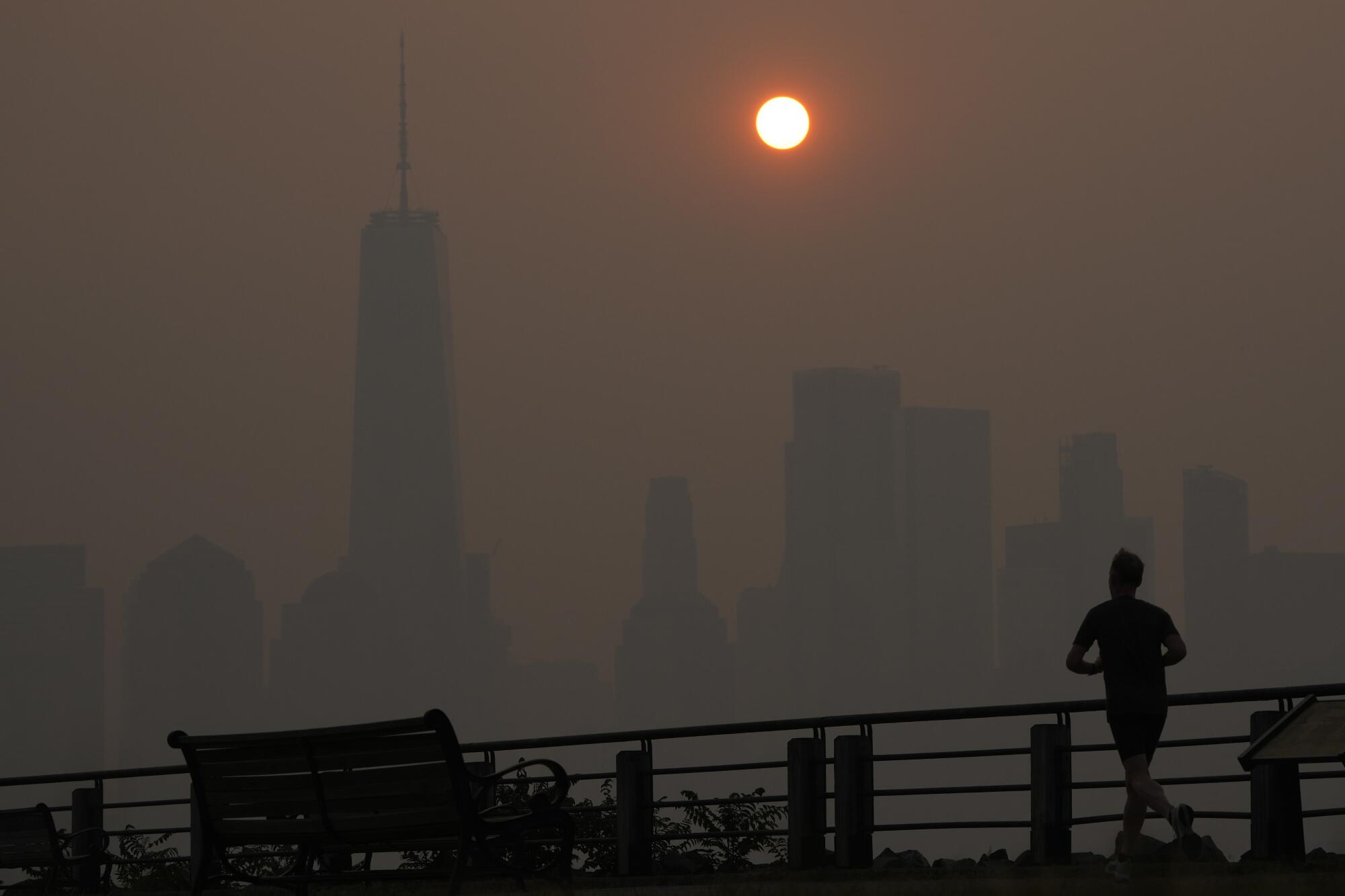 A man runs along a path as the sun rises amid haze over a skyline.