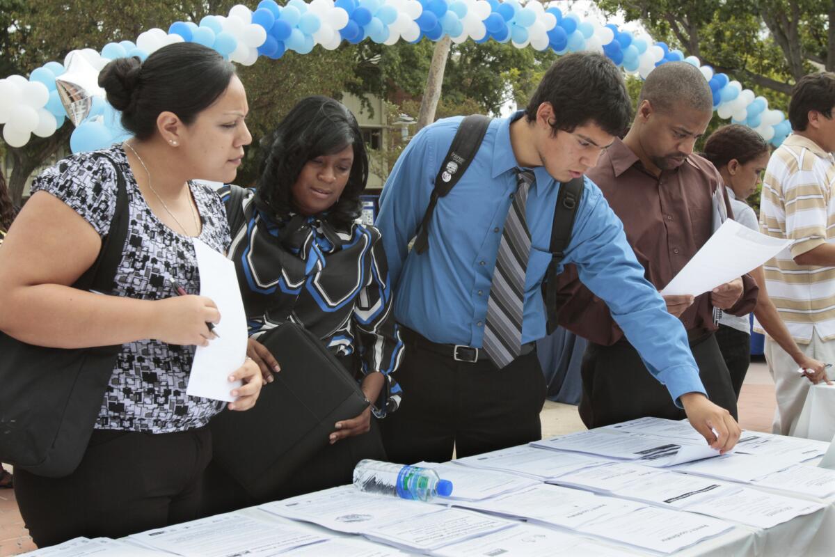 Applicants look over offerings at a jobs fair. Los Angeles County will continue its slow-and-steady economic recovery in 2014 and 2015, a report says.