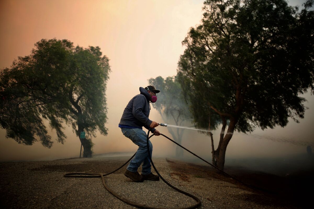 Billy MacFarlane uses a garden hose to douse embers on his family’s ranch