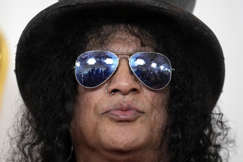 Slash puckers his lips while wearing a large black hat and aviator glasses