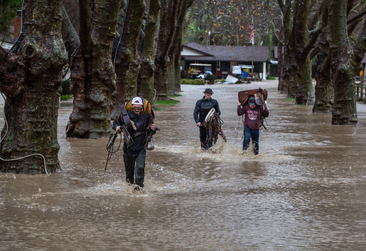Men carry saddles and other horse tack on a flooded road.
