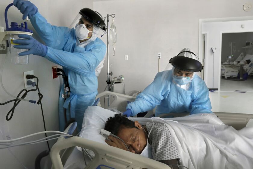 HOUSTON, TEXAS-MAY 6, 2020-Alan Araiza (left) sets up oxygen equipment for newly arrived COVID patient Angel Rodriguez, 40, with nurse Anita Pedy (right). In Houston, Texas at United Memorial Medical Center, Dr. Joseph Varon leads a team of nurses and medical students in the Covid-19 unit. (Carolyn Cole/Los Angeles Times)