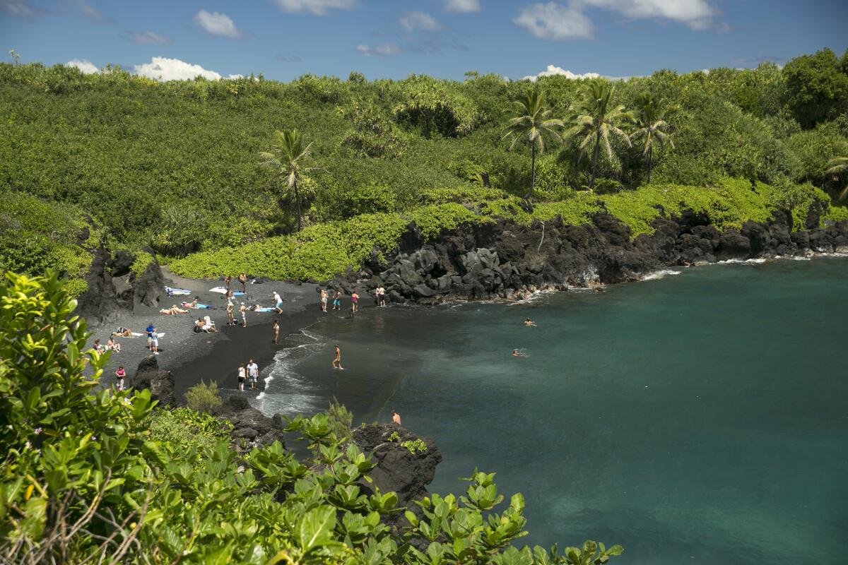 People on the black sand beach at Waianapanapa State Park in Hana, Hawaii